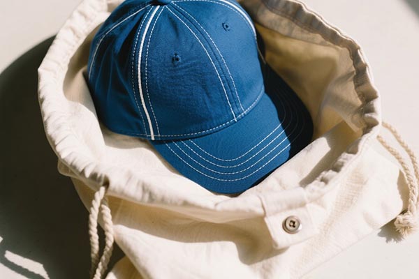 Blue baseball cap inside a cream-colored drawstring bag.