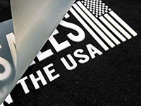 Close-up of heat transfer vinyl peeling off black fabric with white text.