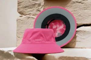 Pink bucket hat with perforations and patterned inner lining displayed on stone surface.