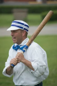 Man wearing retro blue and white baseball cap holding wooden bat outdoors.