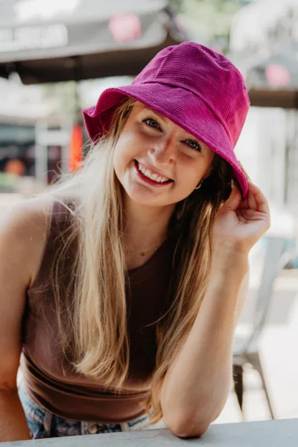 Smiling woman wearing a raspberry pink corduroy bucket hat outdoors.