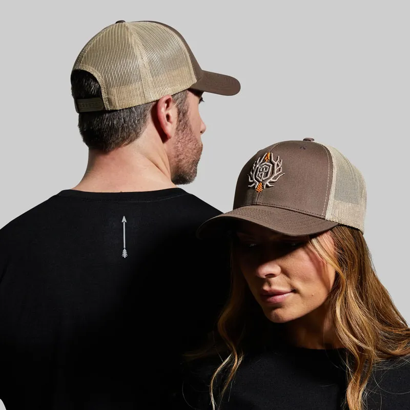Man and woman wearing brown trucker hats with mesh back and embroidered logo.