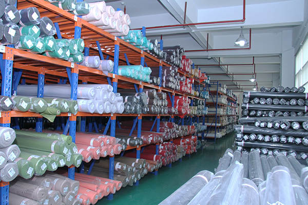 Rolls of various colored fabrics stored on metal shelves in warehouse.