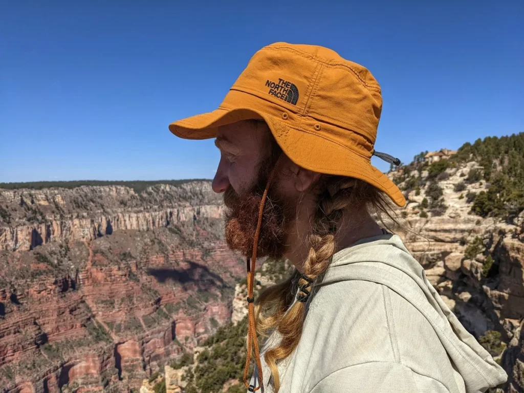 Man with braided hair wearing orange hat overlooking rocky canyon.