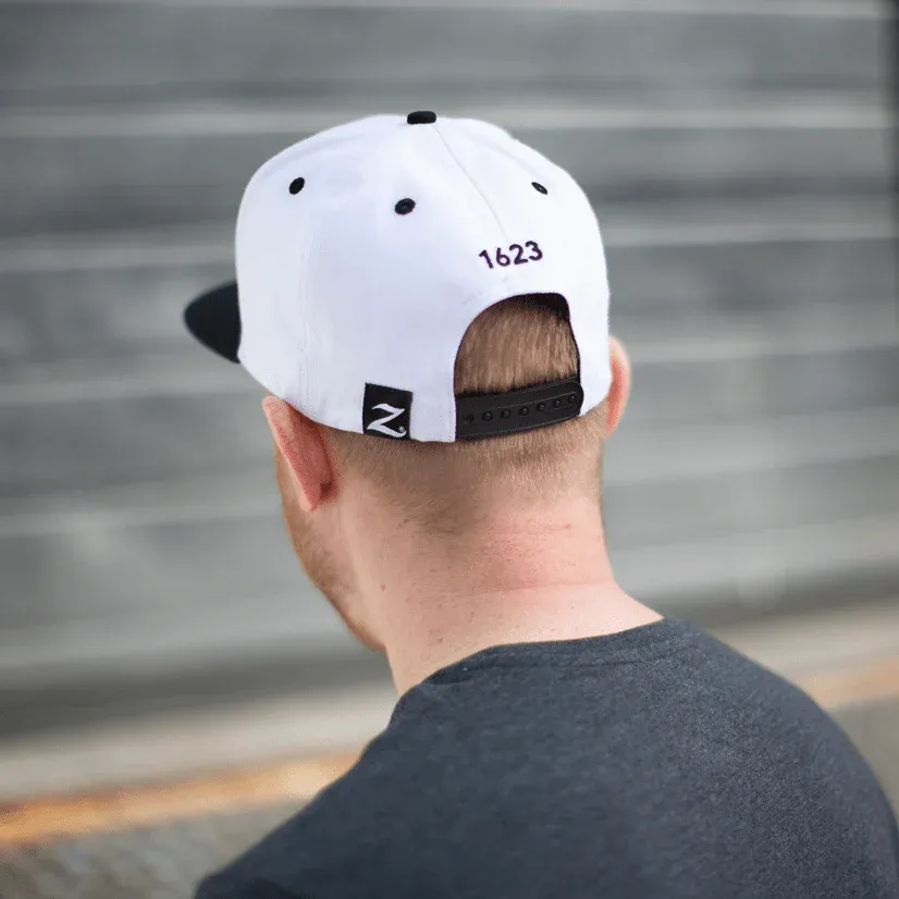 Rear view of man wearing white snapback hat with black adjustable strap outdoors.