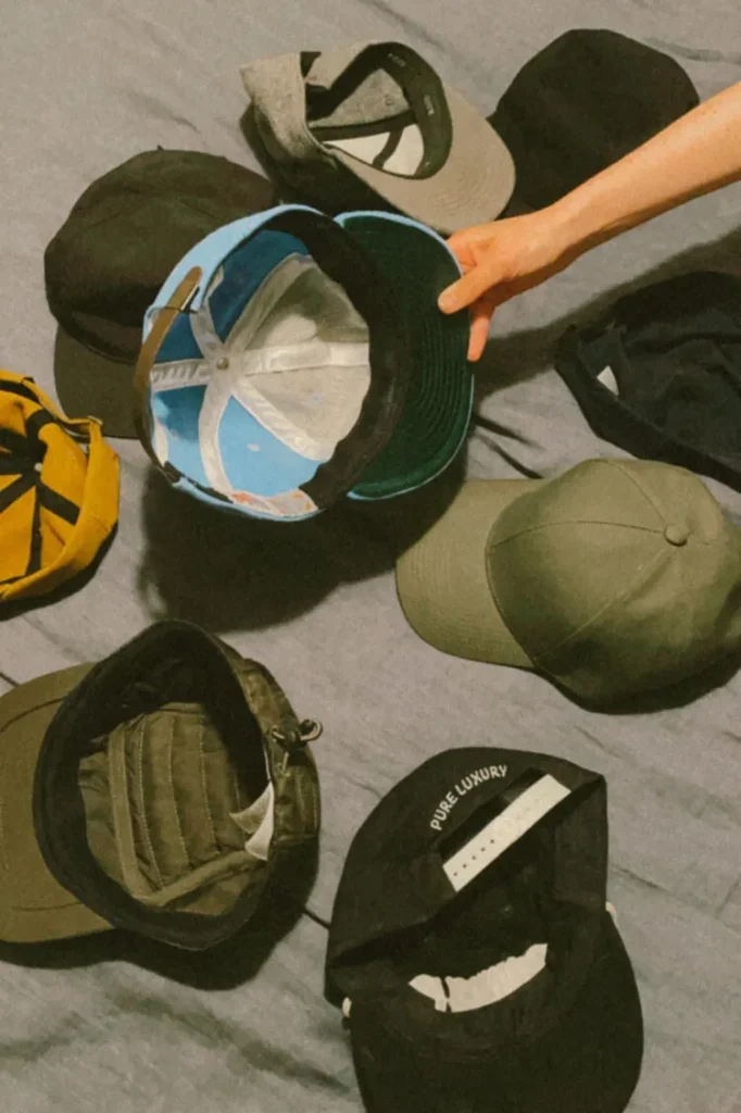 Various baseball caps laid out on a surface with a hand holding one cap.