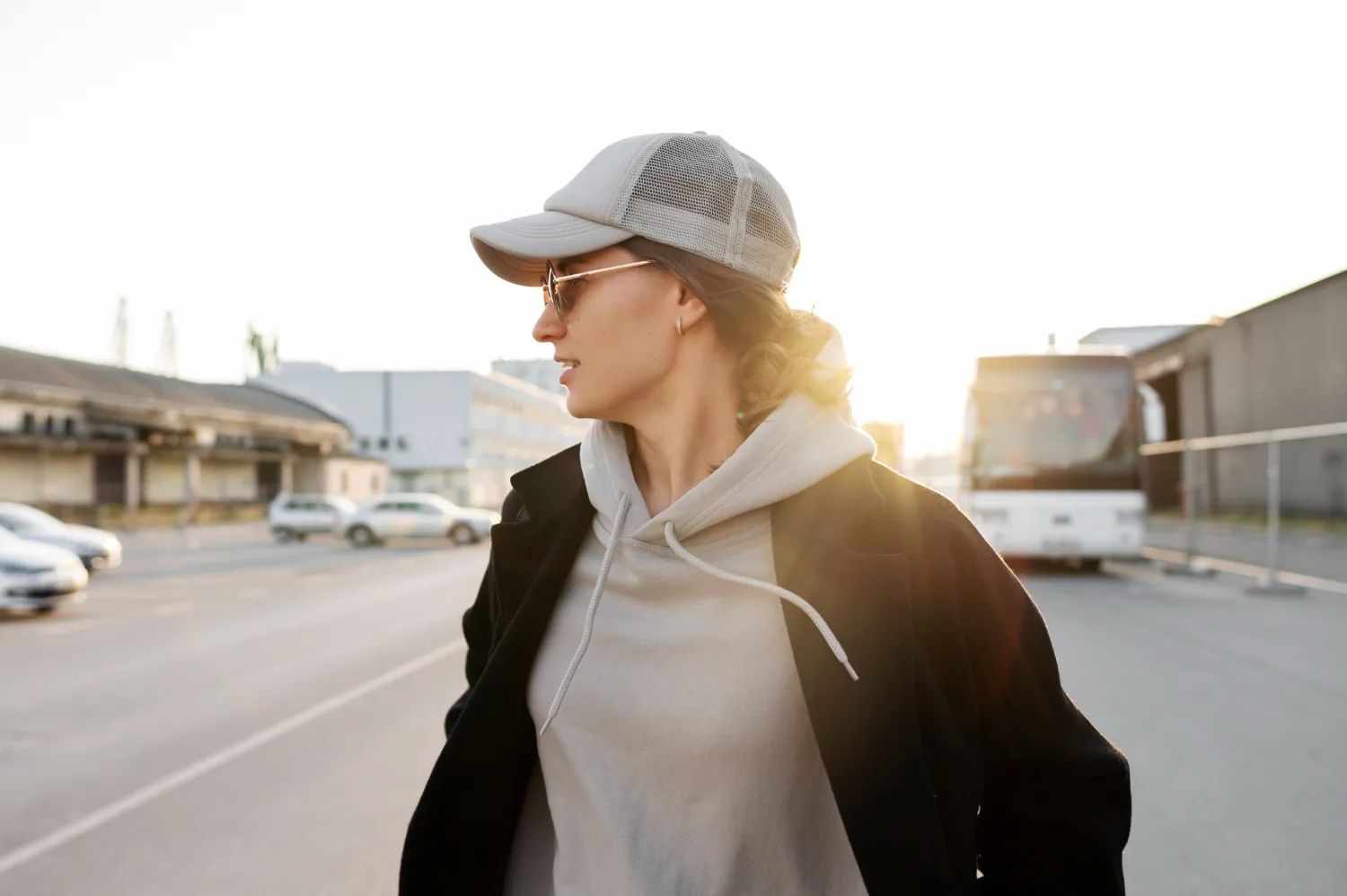 Woman wearing grey trucker hat and sunglasses, walking in the sun.