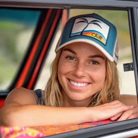 Woman smiling wearing a trucker hat with a palm tree and "Chill" design.