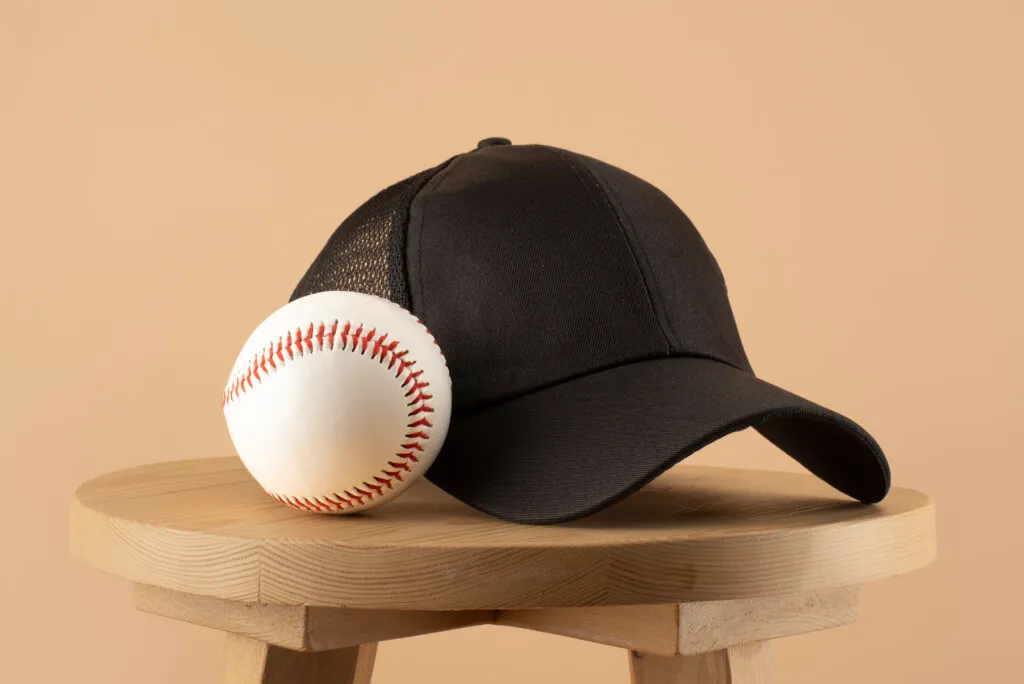 Black baseball cap placed next to a white baseball on wooden stool.