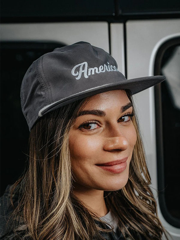 Smiling woman with long hair wearing gray baseball cap with text.