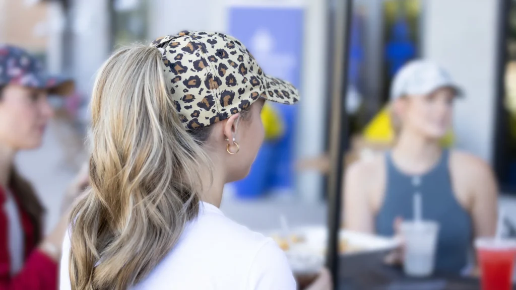 Woman wearing leopard print baseball cap with ponytail, sitting at a table with friends.