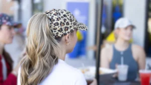 Woman wearing leopard print baseball cap with ponytail, sitting at a table with friends.