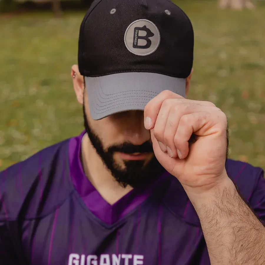 Man wearing black and grey baseball cap with circular "B" logo outdoors