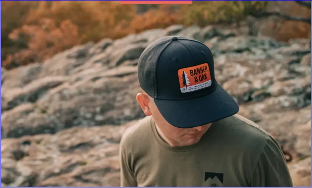 Man wearing black fitted hat with orange patch outdoors