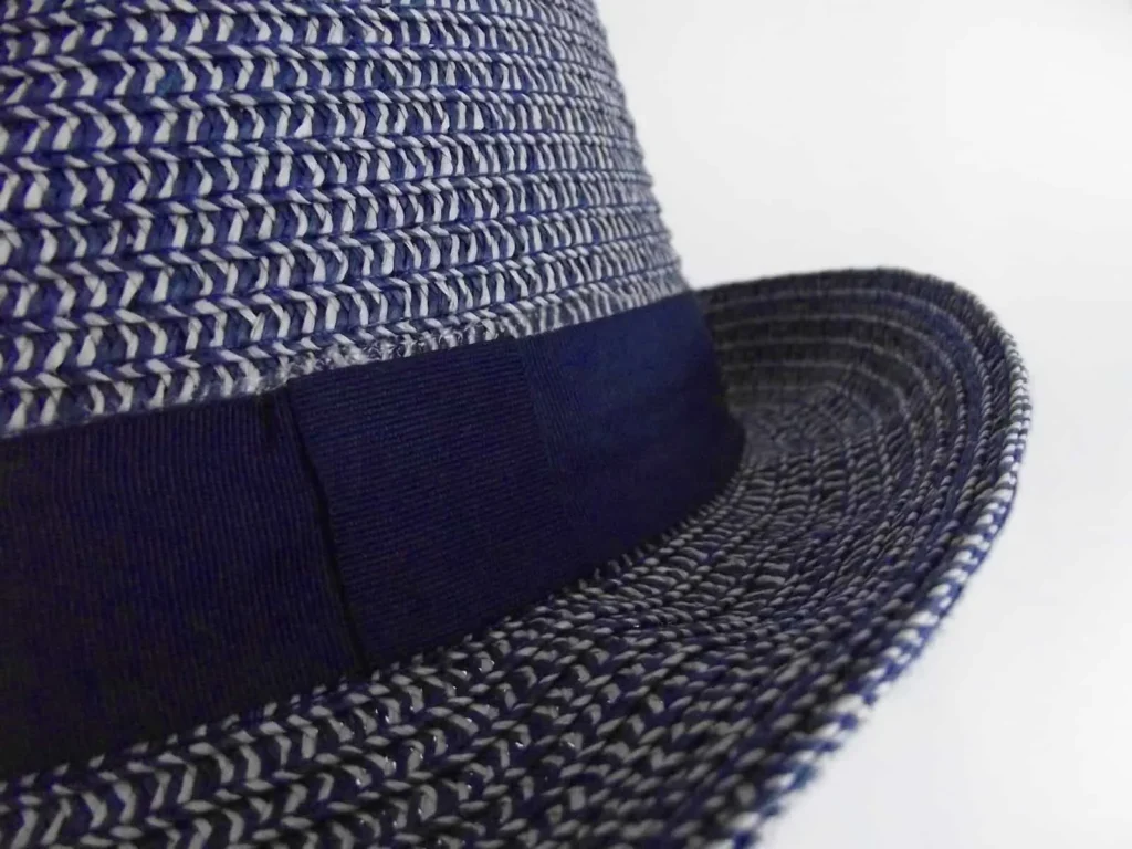 Close-up of a woven straw hat with a navy blue band, showing the intricate texture of the brim.