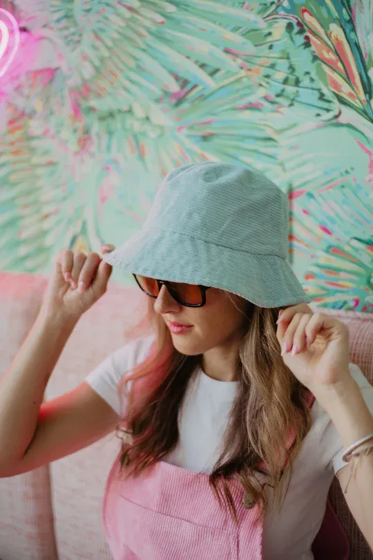 Woman wearing a mint bucket hat and sunglasses indoors.