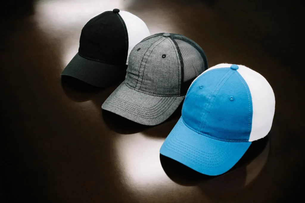 Black, grey, and blue-white trucker hats displayed on dark reflective surface.