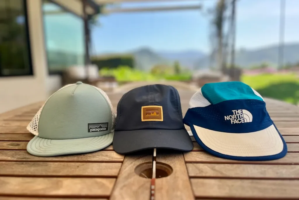Three outdoor caps from Patagonia and The North Face on wooden table.