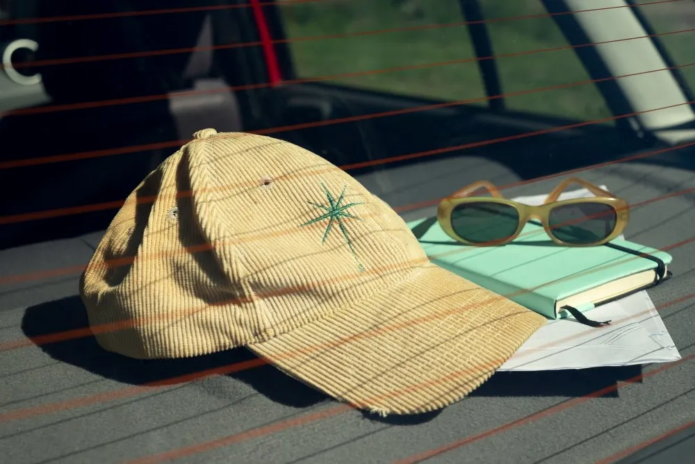 Corduroy hat with a green embroidery star, sunglasses, and a notebook on a car seat.