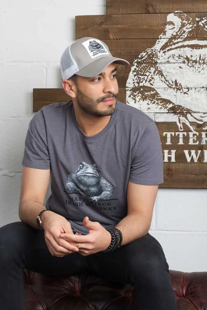Man wearing a gray trucker hat with frog logo, sitting on a couch with a graphic backdrop.