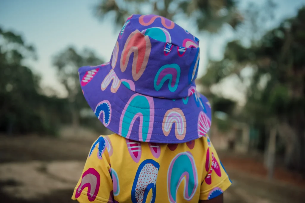 Child wearing a vibrant purple bucket hat with abstract shapes and matching shirt outdoors.