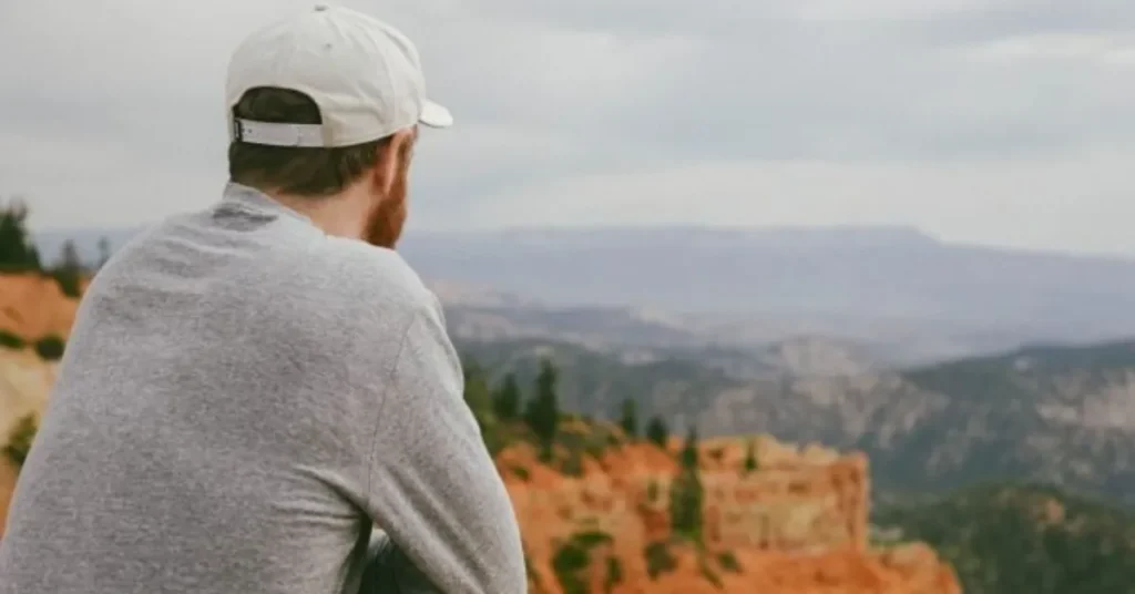 Rear view of man wearing white baseball cap overlooking scenic canyon landscape.