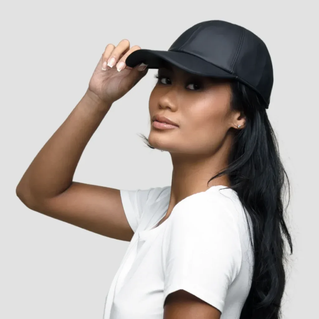 Woman wearing black leather baseball cap and white shirt against gray background