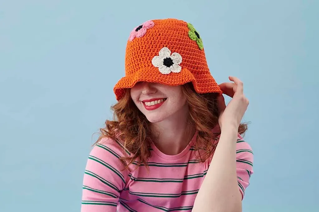 Woman wearing orange crochet bucket hat with flower decorations.