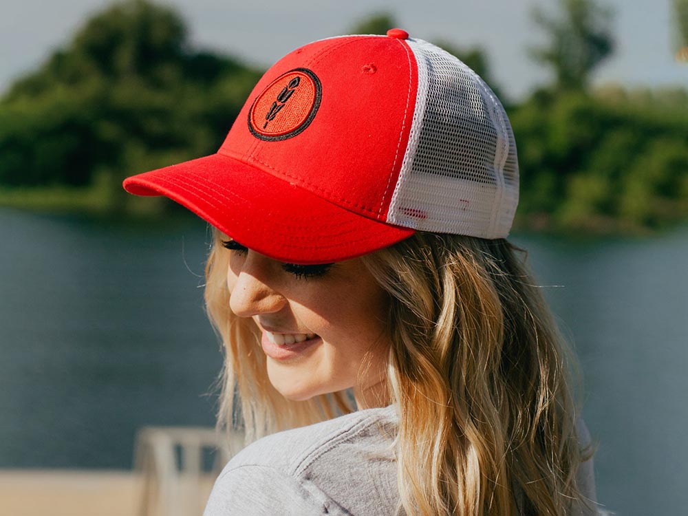 Smiling woman wearing red and white mesh trucker hat outdoors.