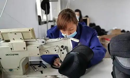 Worker sewing black caps using industrial sewing machine in factory.