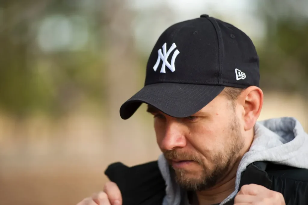 Man wearing black New York Yankees dad hat outdoors adjusting jacket.