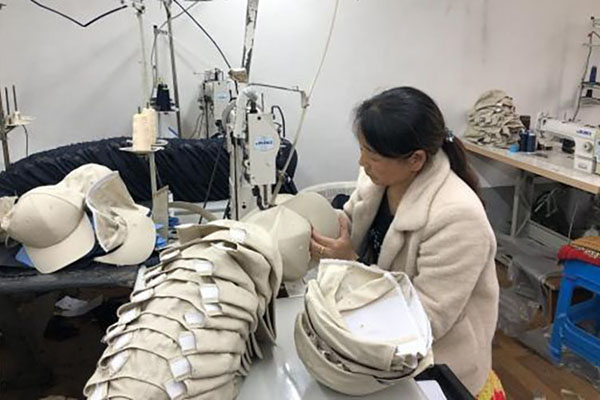 Worker assembling beige caps in a textile factory setting.