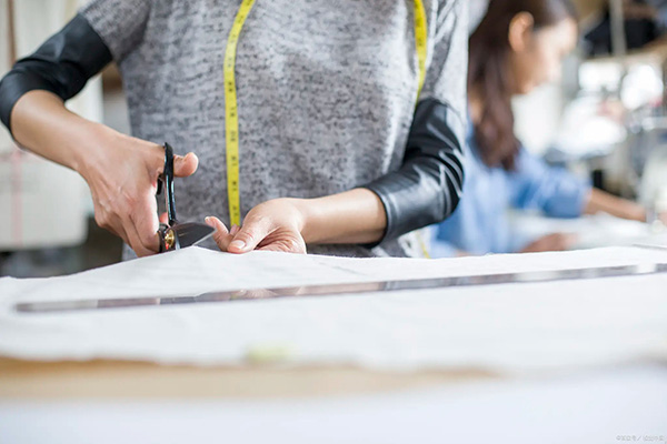 Person cutting fabric with scissors in a sewing workshop.