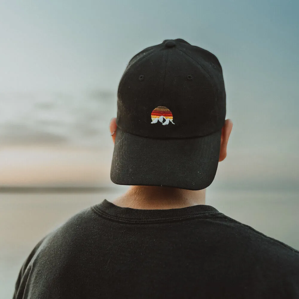 Person wearing black cap with sunset and whelk design viewed from behind.