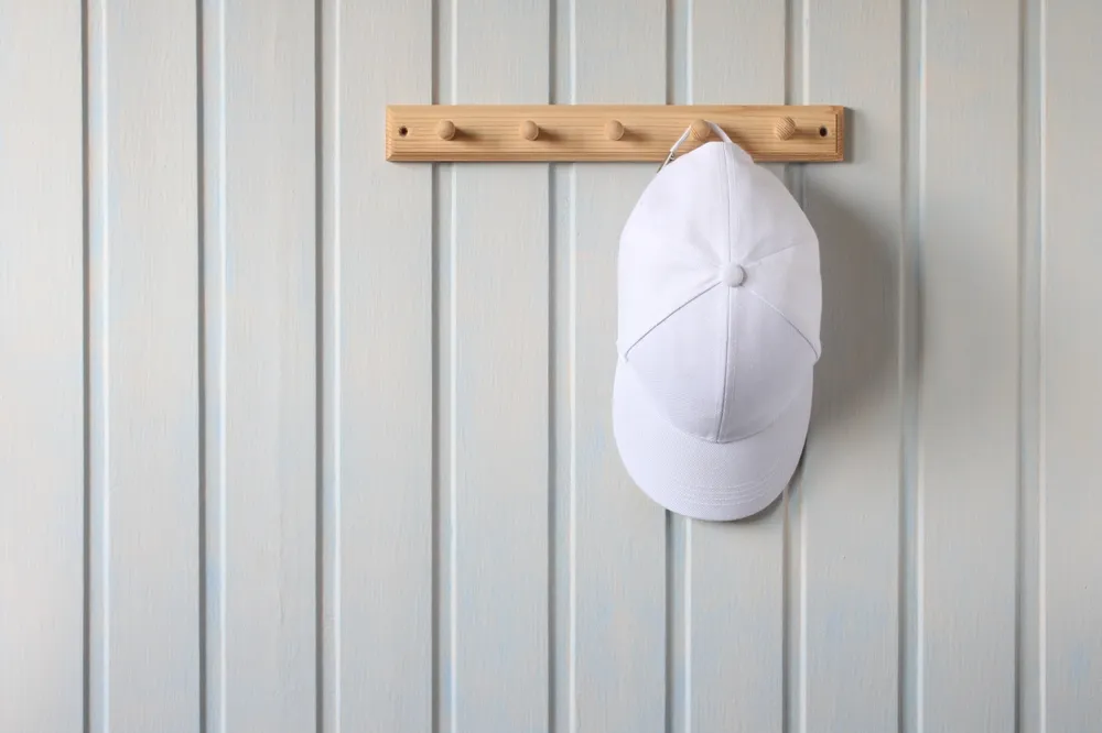 White baseball cap hanging on wooden wall hooks