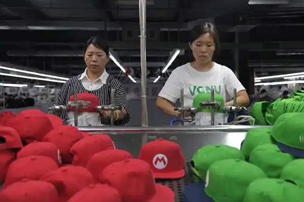Two women working on red and green caps in factory assembly line.