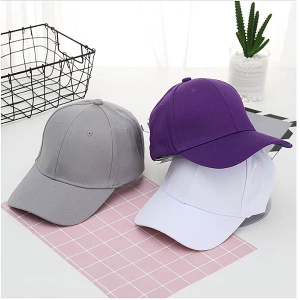 Three caps in gray, purple, and white, neatly placed on a grid-patterned surface with a plant in the background.