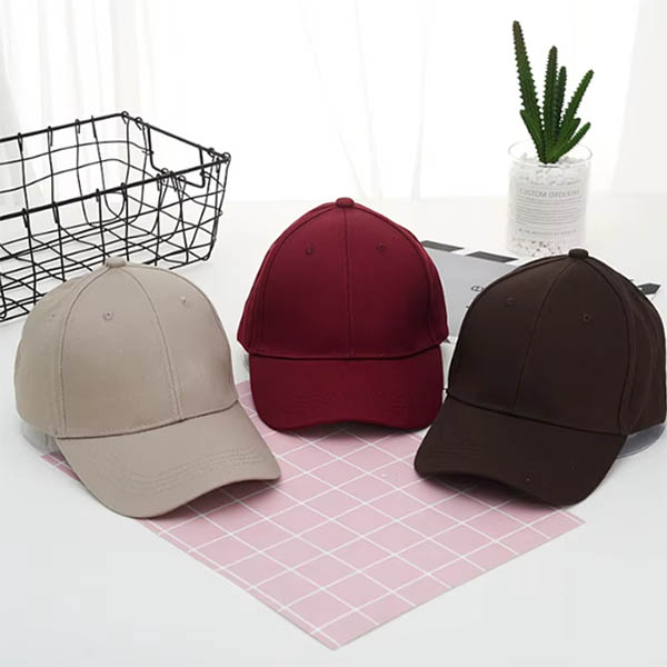 A selection of caps in beige, maroon, and brown arranged on a flat surface with a decorative plant in the background.