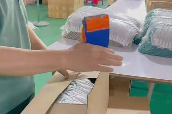 Person packing hat into cardboard box on a white table.