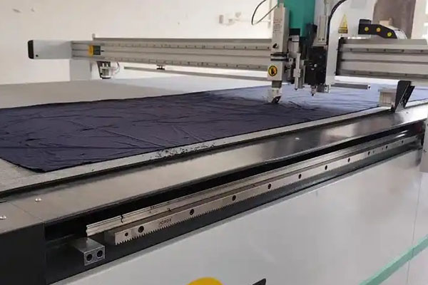 Industrial automated fabric cutting machine slicing black fabric.