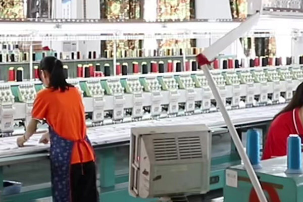 Worker operating large embroidery machine with multiple spools of thread.