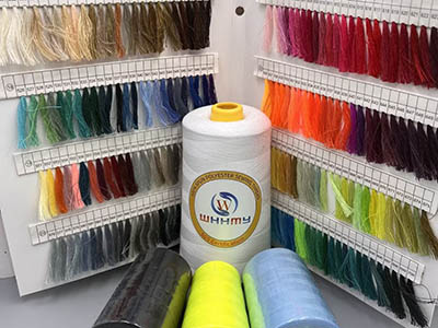 A variety of thread colors displayed in strands on racks with a large spool of white thread in the center.