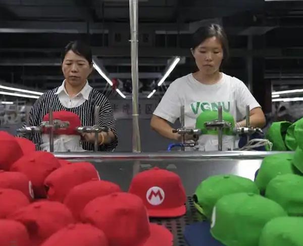 Workers assembling red and green caps on production line in factory.