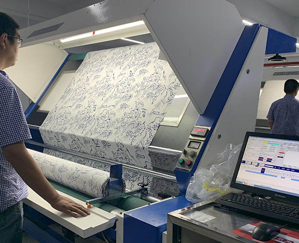 Worker monitoring fabric printing machine with blue floral patterns.