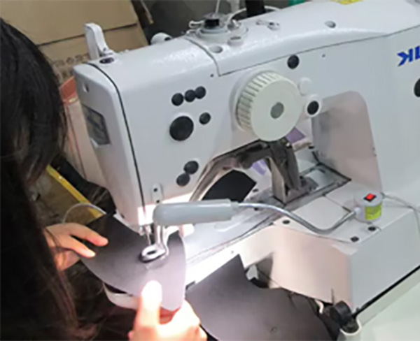 Worker sewing black fabric panels with industrial sewing machine.
