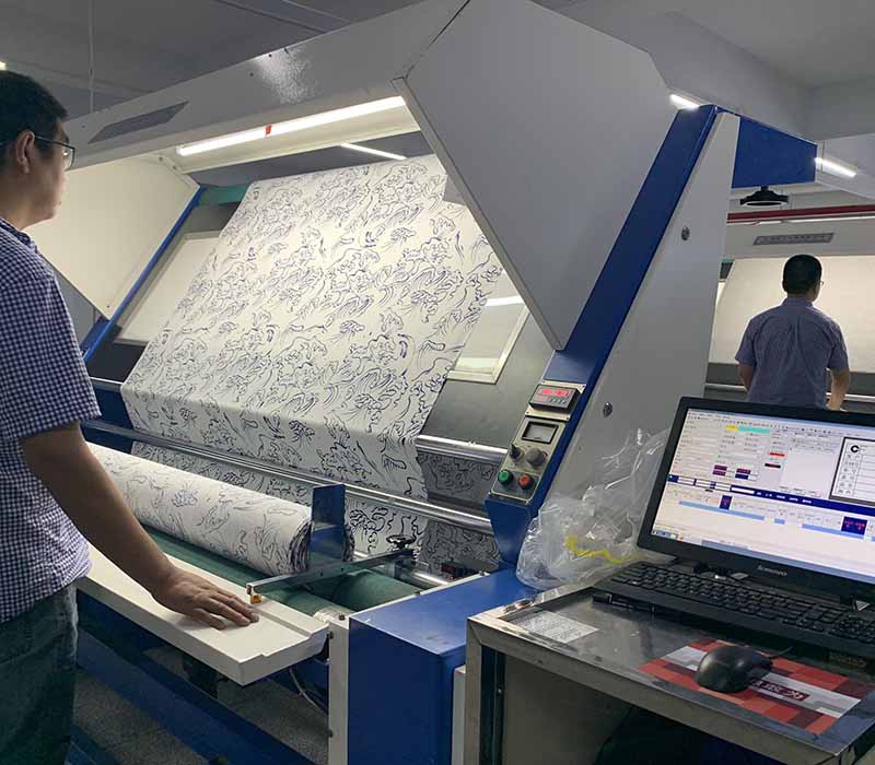Man inspecting printed fabric roll on automated inspection machine.