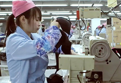 Worker sewing black hat parts on industrial machine in factory.