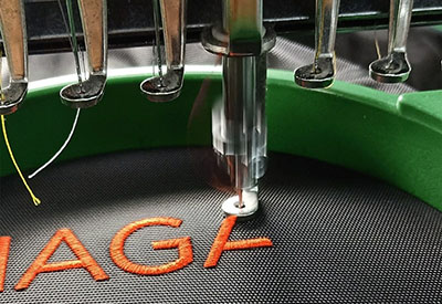 Close-up of embroidery machine stitching orange thread on fabric.
