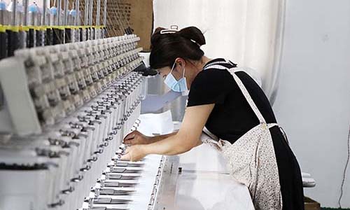 Woman wearing mask working on large embroidery machine.