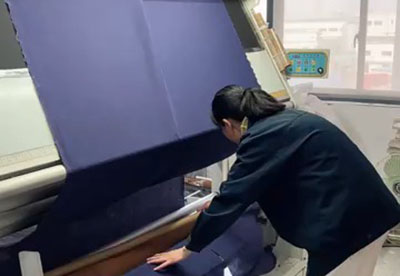 Worker checking large rolls of fabric in factory setting.